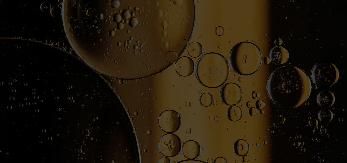 imagen de fondo (oscurecida para que se lea el texto encima, tipo banner. Gotas de aceite dorado flotando en agua sobre fondo oscuro, en primer plano